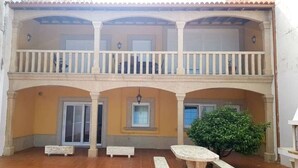 A two-story building with a balcony, a tiled patio, and a small tree. - Casa Do Castillo (Fisterra)