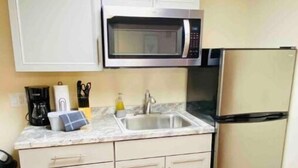 Uma cozinha compacta com armários brancos, micro-ondas de aço inoxidável, geladeira e pia.