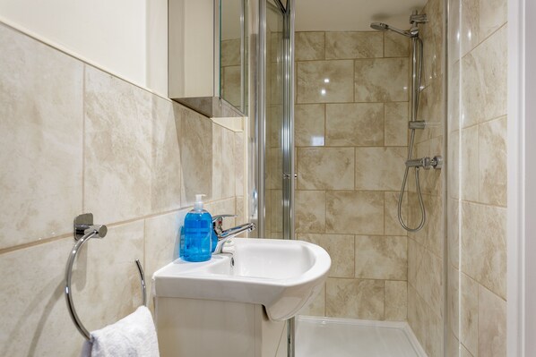 Un baño con lavamanos blanco, cabina de ducha con mampara de vidrio y baldosas color beige.