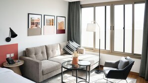 A modern hotel room with a sofa, a chair, a small table, and a large window with curtains. - Dara Hotel Qurtubah (Riyadh)