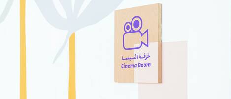 A wooden sign with a camera icon and the text "Cinema Room" in both Arabic and English.