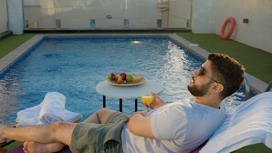 A man relaxing by a pool with a fruit bowl and drink on a small table. - Dara Hotel Qurtubah (Riyadh)