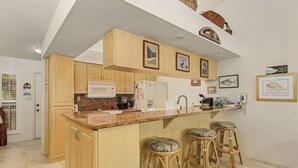 A kitchen with wooden cabinets, a granite countertop, a microwave, a refrigerator, and a bar area with stools.