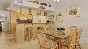 Eine moderne Küche mit Holzausstattung, einer zentralen Kochinsel und einem Essbereich mit Korbstühlen und einem Glastisch.