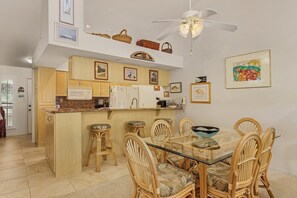 Une cuisine moderne avec des meubles en bois, un îlot central et un coin repas comprenant des chaises en osier et une table en verre.