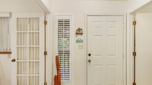 A hallway with a white door, a window with blinds, and a small shelf with a decorative item.
