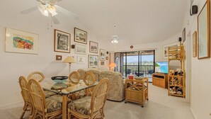 A living room with a glass dining table, wicker chairs, a sofa, and a TV.