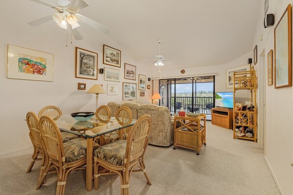 A living room with a glass dining table, wicker chairs, a sofa, and a TV.