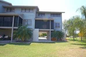A two-story building with a covered parking area and a grassy lawn. - Corner Condo in Blue Crab Key, Bokeelia! (Saint James City)