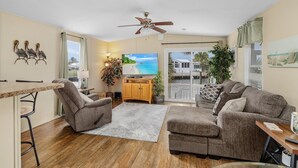 A living room with a sofa, armchairs, a TV, a wooden cabinet, and a ceiling fan.