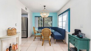 A compact kitchen with a dining area, a refrigerator, wicker chairs, a blue sofa, and a small table with drawers. - Blue Crab Key Condo with Amazing Water Views! (Saint James City)