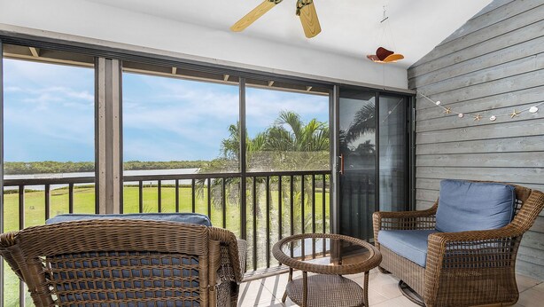 A balcony with wicker furniture, a ceiling fan, and a view of a green landscape. - Blue Crab Key Condo with Amazing Water Views! (Saint James City)