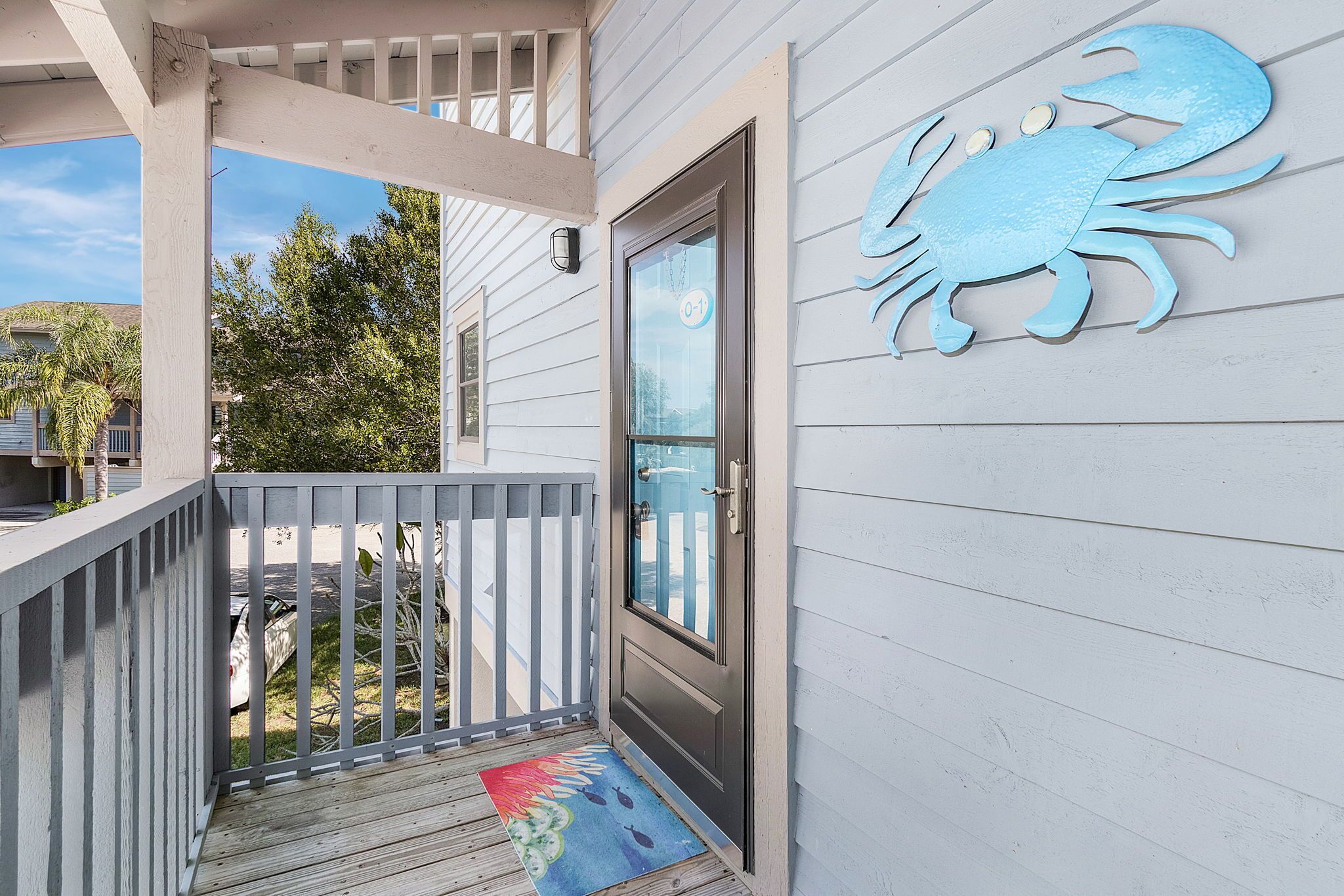A wooden porch with a white railing, a glass door, and a blue crab decoration on the wall.