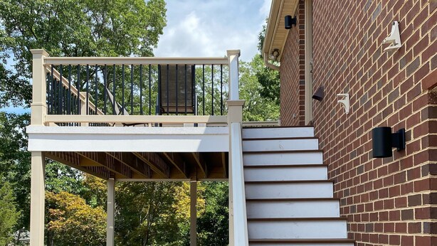 Eine Holzterrasse mit einer Treppe, die zu einem überdachten Bereich mit Gartenmöbeln führt.