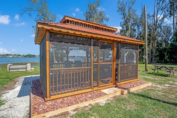 A wooden structure with glass doors and windows, located near a body of water and a picnic area.