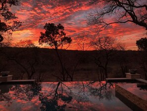 Ein Sonnenuntergang mit einem Pool, der den Himmel spiegelt, umgeben von Bäumen und einer Steinstruktur.