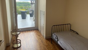 Ein Schlafzimmer mit einem Einzelbett, einem kleinen Tisch und Blick auf einen Balkon mit Stühlen und einem Tisch.