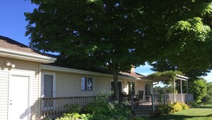 Ein eingeschossiges Haus mit überdachter Veranda, einem kleinen Garten mit verschiedenen Pflanzen und einer Rasenfläche.