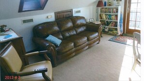 A living room with a brown leather sofa, a wooden chair, a bookshelf, and a small table. - Quiet Getaway Within Walking Distance of the Beach and Mall. (Cape May)