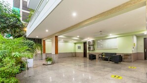 A spacious lobby with a high ceiling, a reception desk, seating area, and indoor plants. - Central Stay, Medical Ease 2BHK (Gurugram)