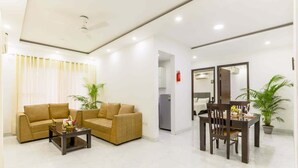 A modern living room with a sofa set, a coffee table, and a dining table with chairs. - Central Stay, Medical Ease 2BHK (Gurugram)