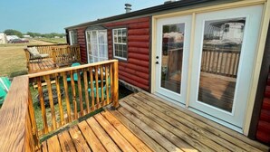 A wooden deck with a bench, a sliding glass door, and a small outdoor seating area. - Private Tiny Home with deck, fire pit & patio near Platte Creek Recreation area (Platte)