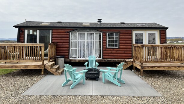 A wooden cabin with a deck, two Adirondack chairs, and a large window. - Private Tiny Home with deck, fire pit & patio near Platte Creek Recreation area (Platte)