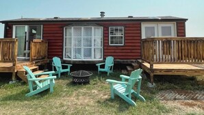 A red cabin with a deck, two turquoise Adirondack chairs, and a fire pit. - Private Tiny Home with deck, fire pit & patio near Platte Creek Recreation area (Platte)