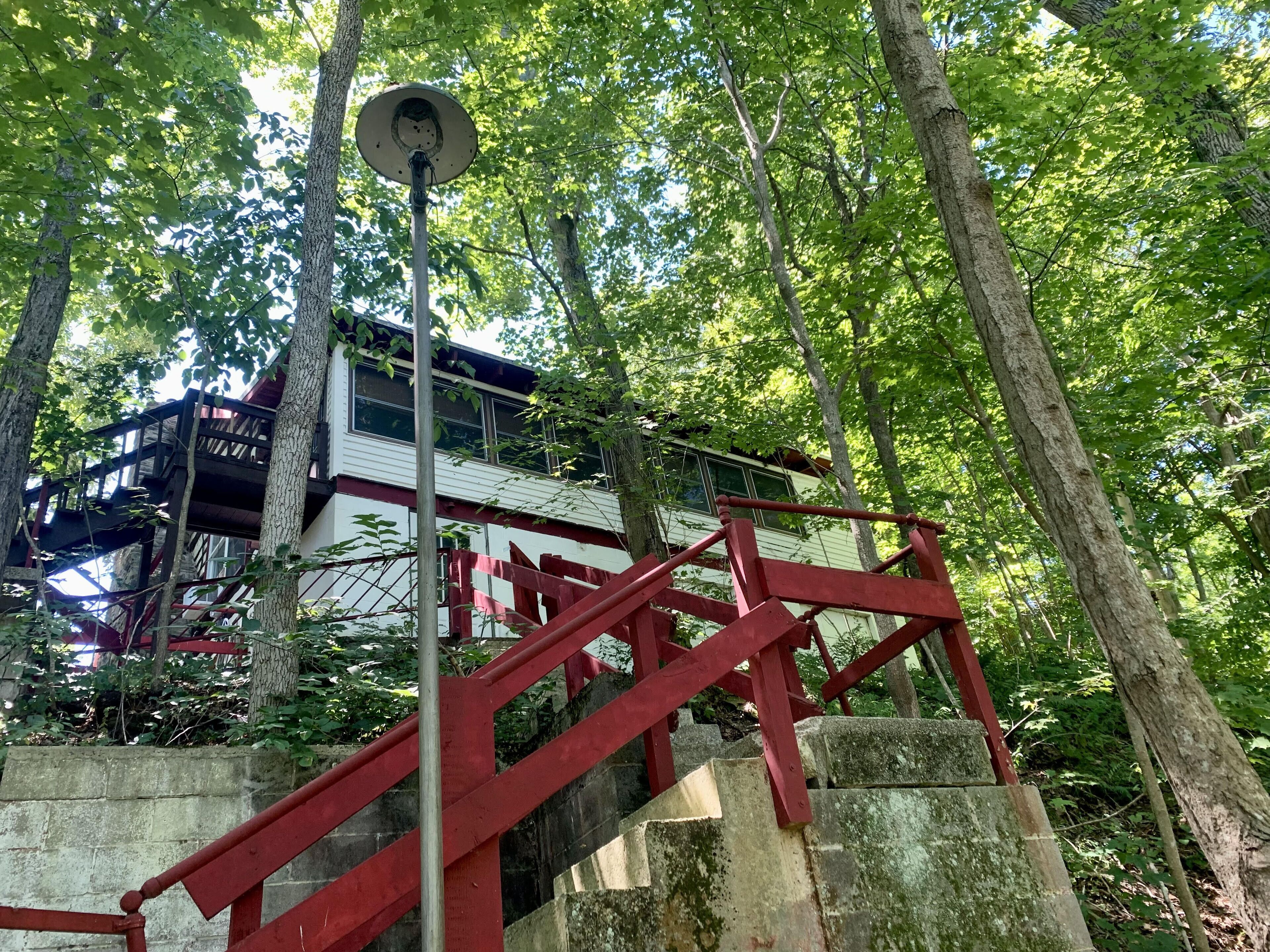 Eine Treppe mit roten Geländern führt zu einem von Bäumen umgebenen Gebäude.