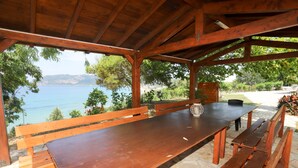A wooden table and benches under a covered area with a view of a body of water and greenery. - Agios Georgios - 2 Beds - Sleeps 5 - Free Parking (Corfu)