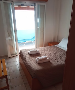 Relax in this inviting room with a large bed, nightstand, and bench, plus a sliding door to an outdoor area with a chair.