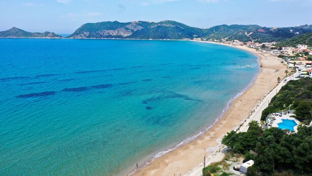 A coastal beach with clear blue waters, a sandy shore, and a pool area. - Agios Georgios - 2 Beds - Sleeps 5 - Free Parking (Corfu)