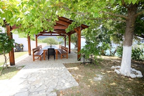 Relax under the shade of a pergola surrounded by lush greenery and a wooden table for al fresco dining.