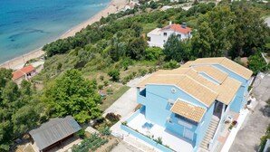 A coastal property with a large blue house, a small adjacent structure, and a beach view. - Agios Georgios - 2 Beds - Sleeps 5 - Free Parking (Corfu)