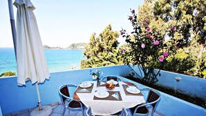 Mesa posta para dois com vista para o mar, um guarda-sol branco e um vaso de flores.