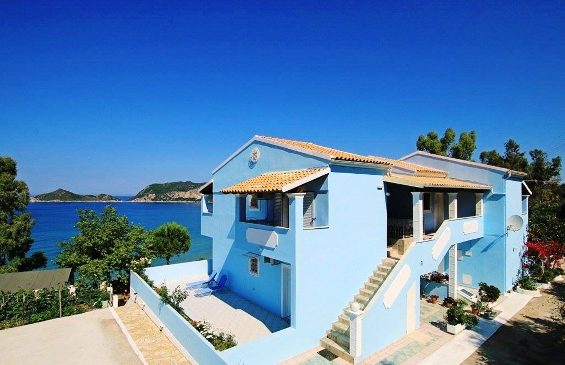 Une maison bleue avec un escalier menant à l’entrée, située au bord d’un plan d’eau sous un ciel dégagé.