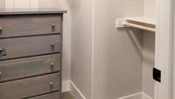 A small, neatly organized closet with a wooden dresser, shelves, and hanging space.