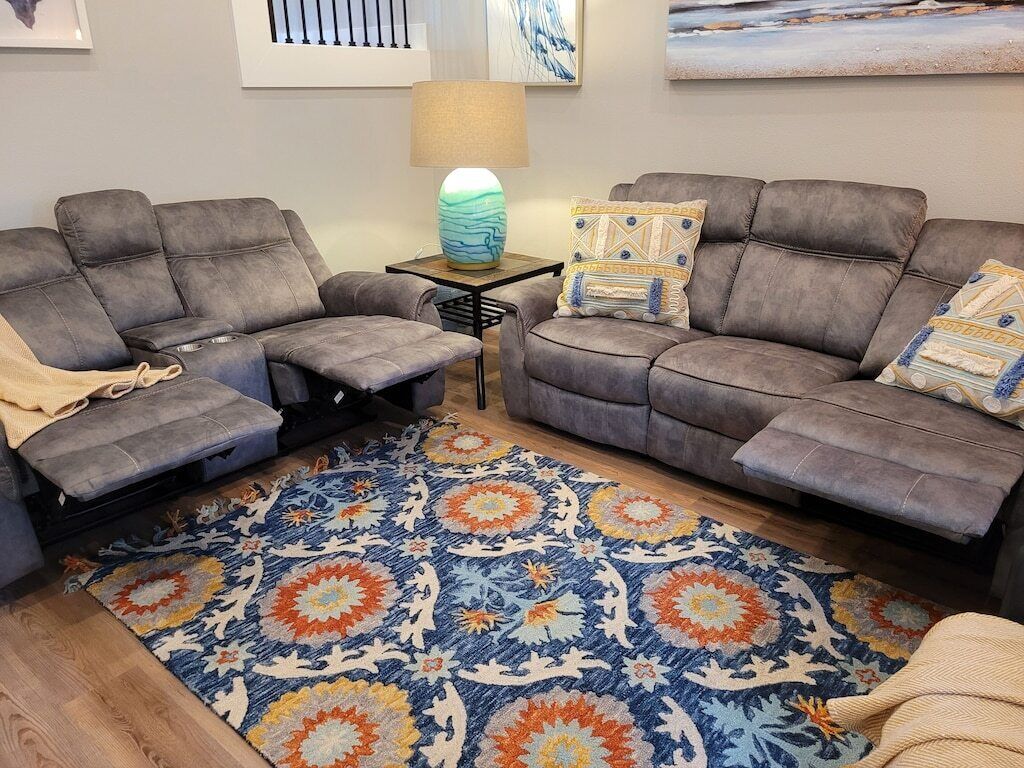 Ein Wohnzimmer mit zwei grauen Sofas, einem gemusterten Teppich und einem kleinen Tisch mit einer Lampe.
