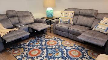 Ein Wohnzimmer mit zwei grauen Sofas, einem gemusterten Teppich und einem kleinen Tisch mit einer Lampe.