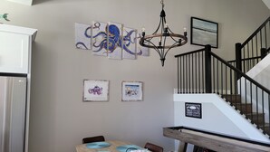 Een eetgedeelte met een houten tafel, blauwe placemats en een wand met kunstwerken.