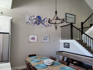 Een eetgedeelte met een houten tafel, blauwe placemats en een wand met kunstwerken.