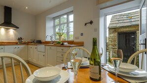 Une cuisine moderne avec des meubles blancs, une cheminée en pierre et une table à manger dressée pour deux personnes, avec des verres à vin et une bouteille.