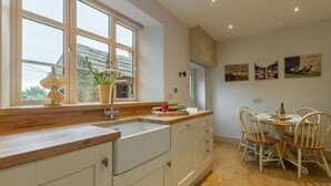 Une cuisine moderne avec un plan de travail en bois, des armoires blanches et une fenêtre donnant sur l’extérieur. On y trouve également un coin repas avec une table et des chaises.