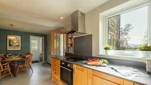 A modern kitchen with wooden cabinets, a black countertop, and a window with a view of greenery. - 1 Riverside Cottage, Burnsall, Yorkshire Dales (Burnsall)
