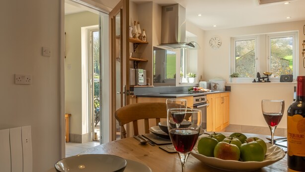 A modern kitchen with a dining table set for two, featuring a bowl of green apples and two wine glasses. - 1 Riverside Cottage, Burnsall, Yorkshire Dales (Burnsall)