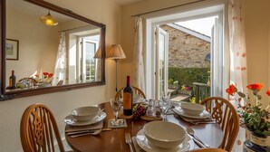 A dining area with a table set for four, a wine bottle, and a mirror reflecting the room. - Fox Cottage, Middleham, Yorkshire Dales (Middleham)