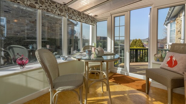 A sunlit room with a glass table, wicker chairs, and a view of a garden through large windows. - Fox Cottage, Middleham, Yorkshire Dales (Middleham)