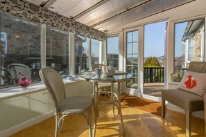 A sunlit room with a glass table, wicker chairs, and a view of a garden through large windows. - Fox Cottage, Middleham, Yorkshire Dales (Middleham)