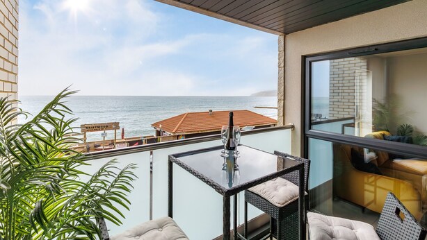 Ein Balkon mit Glastisch, Stühlen und Meerblick.