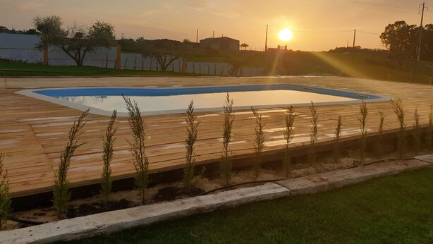 Ein rechteckiger Pool mit umlaufender Holzterrasse vor einem Sonnenuntergangshimmel.
